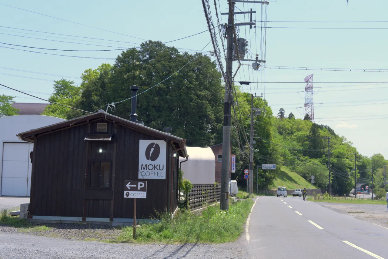 道路沿いに立つMOKU COFFEEの外観。黒い板張りの建物と、駐車場を示す「P→」の看板。
