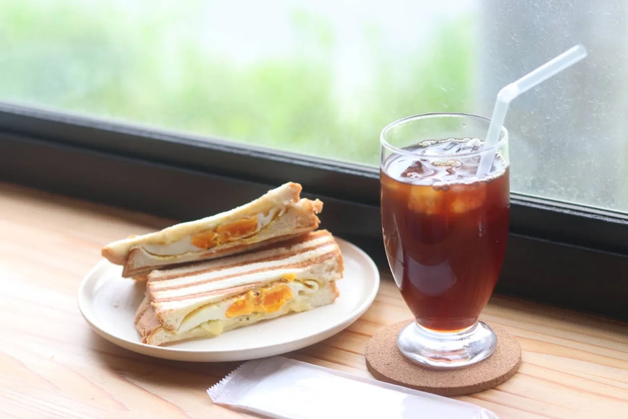 窓辺の席に置かれた、卵入りのホットサンドとアイスコーヒー。